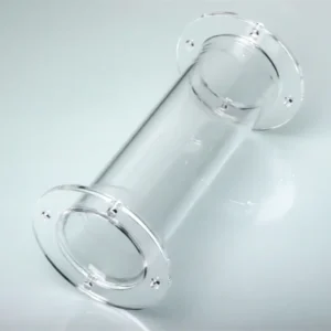 A transparent quartz tube with two precision-machined flanges, each with multiple bolt holes, standing vertically on a reflective light-colored surface.