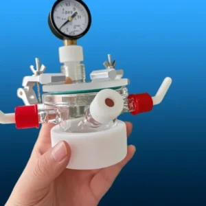A hand holding a fully assembled quartz photocatalytic reactor with a pressure gauge, demonstrating its compact size and various functional ports.