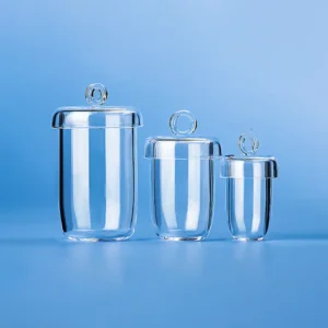 Three clear quartz glass crucibles of varying sizes, each with a lid featuring a loop handle, displayed on a blue background.