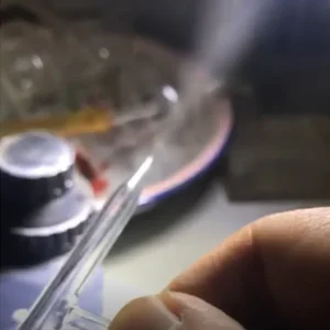 A hand holding the tip of a quartz atomizing spray nozzle, with a faint spray or mist visible, suggesting its atomization function during operation.